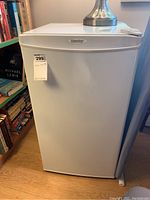 Photo of the Danby fridge exterior showing white door with brand logo and a sticker with measurements noted.