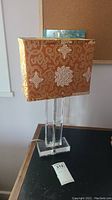 Front and side views of the table lamp showing the clear glass base and ornate orange and gold patterned fabric shade.