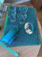 All items displayed on table with turquoise place mat beneath, showing 4 glasses, gravy boat, and crystal gem