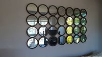 Front view of the large wall mirror display showing all 24 round mirrors arranged in a grid pattern and framed in dark metal.