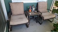 Two outdoor metal chairs with beige patterned seat and back cushions next to small square tile top metal frame side table on porch.