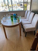 Oval dining table with removable leaf, surrounded by four cream upholstered chairs, sunlit room with window view.