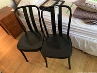 Two black metal chairs positioned side by side on a wooden floor near a bed and nightstand.