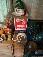 Photo showing green and white baseball caps stacked on a box with various items around including metal wire cap holders and drapes