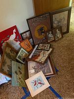 Multiple framed and unframed art pieces grouped together on the floor, showing wildlife and outdoor scenes, plus portraits of children.