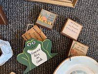 Photo showing five small decorative signs including a frog-shaped 'Forever Relax On God' sign, and signs with inspirational phrases and rustic designs