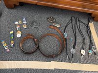Full view of lot content including belts, buckles, bollos, pins, and ring laid on carpeted floor.