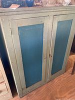 Front view of two-door wooden cabinet with blue inset panels and chipped paint.