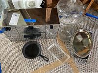 View of three metal canisters, cast iron skillet pan, glass cake plate with dome, glass bowls, and metal trays arranged on carpet.
