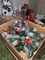 Glass hurricane candle holder atop Christmas wreath with holly, berries, and faux pine branches.