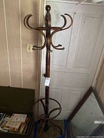 Full view of wooden coat rack with top coat hooks and umbrella ring at bottom.