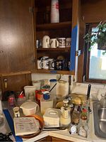 Photo of kitchen counter and cabinet showing various kitchenware including pitchers, Tupperware, mugs, and scales