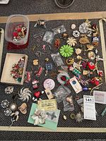 Full lot overview showing a variety of assorted pins and brooches including some in small containers and loose on a carpeted floor.