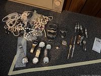 Photo displaying multiple men's and women's wristwatches alongside several beaded necklaces on carpeted surface.