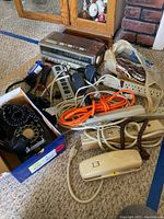 Photo showing York 8-track player, various power strips, extension cords, black rotary wall phone, and other assorted electronic accessories on carpeted floor