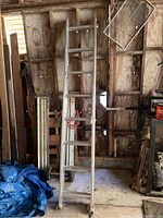 Full view of Werner aluminum extension ladder standing upright in garage against a wooden wall.