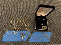 Lot laid out on carpet includes two gold plated bracelets, a gold plated necklace with cross pendant, and a boxed 14K marked earring and pendant set.