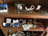 Overview photo of assorted men's accessories and costume jewelry laid out on wooden shelves including wallets, earrings, necklaces, and rings.