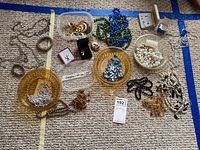Full overview of costume jewelry lot arranged on carpet background showing various chains, faux pearl strands, beads, angel pendants, and small boxed earrings.