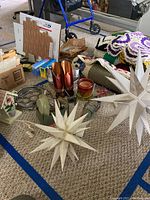 Table with various items including two white decorative lighted star ornaments made of lightweight material, candles in glass holders, crochet doilies, and candle snuffers.