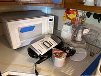 GE white microwave oven, food processor, and George Foreman grill on kitchen counter with accessories and owner's manual shown