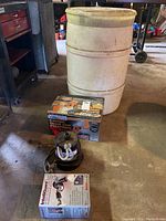Photo showing submersible utility pump, plastic barrel, and boxed Chicago Electric chainsaw sharpener arranged on garage floor.