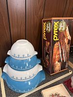 Four nested Pyrex blue and white bowls stacked, showing alternating colors and floral pattern, beside the Pyrex Bake-A-Round box