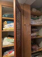 Shelves filled with folded linens including table cloths, napkins, towels, blankets, and sheets in various colors and fabrics.