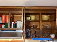 Wood kitchen cabinet with shelves filled with various bowls and containers. Includes vintage glass bowls and candy dishes as well as some plastic containers.