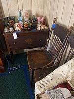 Photo showing vintage wooden cabinet with decorative carved drawer front, various small decorative items on top, and two matching wooden chairs with carved inlay seats.