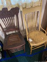 Photo showing both vintage spindle back wood chairs side by side, highlighting the carved dark wood chair with cane seat and the yellow painted chair with broken back.