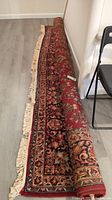 Rolled vintage Karastan area rug with visible floral patterns and cream fringe along edges.