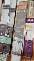 Photo of boxed window coverings showing various brands and types including Allen + Roth cordless shades and Bali vinyl blinds.