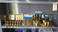 Full shelf view showing an array of brass hardware including window sash locks, hinges, faceplates, hooks, and bolts.