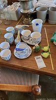 Photo showing blue design china cups and saucers, some ceramic nesting measuring cups with bird print, Japanese style cups and spoons, tumblers and chicken shaped salt and pepper shakers arranged on wooden table.