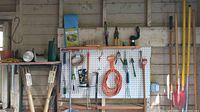 Image showing pegboard with hanging garden tools including extension cord, hand tools, rake and spade on right side and some tools also on shelf to left of pegboard
