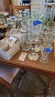 Table with various glassware including clear ice cream glasses, pewter candle holders with etched glass tops, and other glass items.