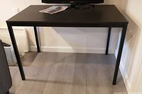 Full view of the IKEA Trend table showing rectangular dark wood finish top and four black metal legs on a floor.