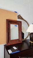 Photo showing the smaller vintage wood framed mirror and corkboard behind it, placed on a dark surface with lamp and larger oval mirror nearby.