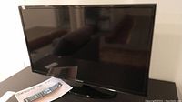Front view of Samsung 32 inch TV turned off, showing screen and included remote on paper.