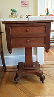 Front view of antique wood side table showing two drawers with round wooden knobs and carved surrounds.