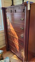 Full front view of wood tall boy dresser with ornate rounded column corners and brass handles.