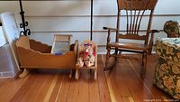 Photo showing wooden doll cradle, miniature washboard, stuffed turkey animal, and small wooden doll chair on wooden floor