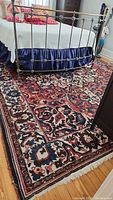 Full view of rug under metal bed frame showing overall pattern, colors, and fringed end