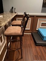 Side view of two beige microfiber bar stools with oil rubbed bronze metal frames placed at a bar counter.
