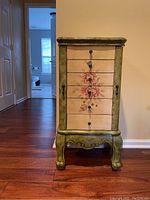 Front view of the painted jewelry armoire showing floral design on drawers and curved legs