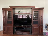 Photo showing the full entertainment unit with two glass-door display cabinets on each side, open central space for TV, drawers and shelves below.