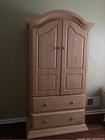 Maple armoire frontal view showing two paneled doors and two drawers beneath with wooden knobs, set against a neutral wall.