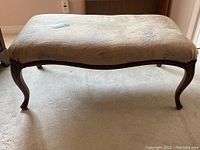 Full view of the bench showing the cloth upholstered top and curved wooden legs with carved details.