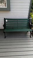 Full front view of the metal framed bench with green wood slats on porch.